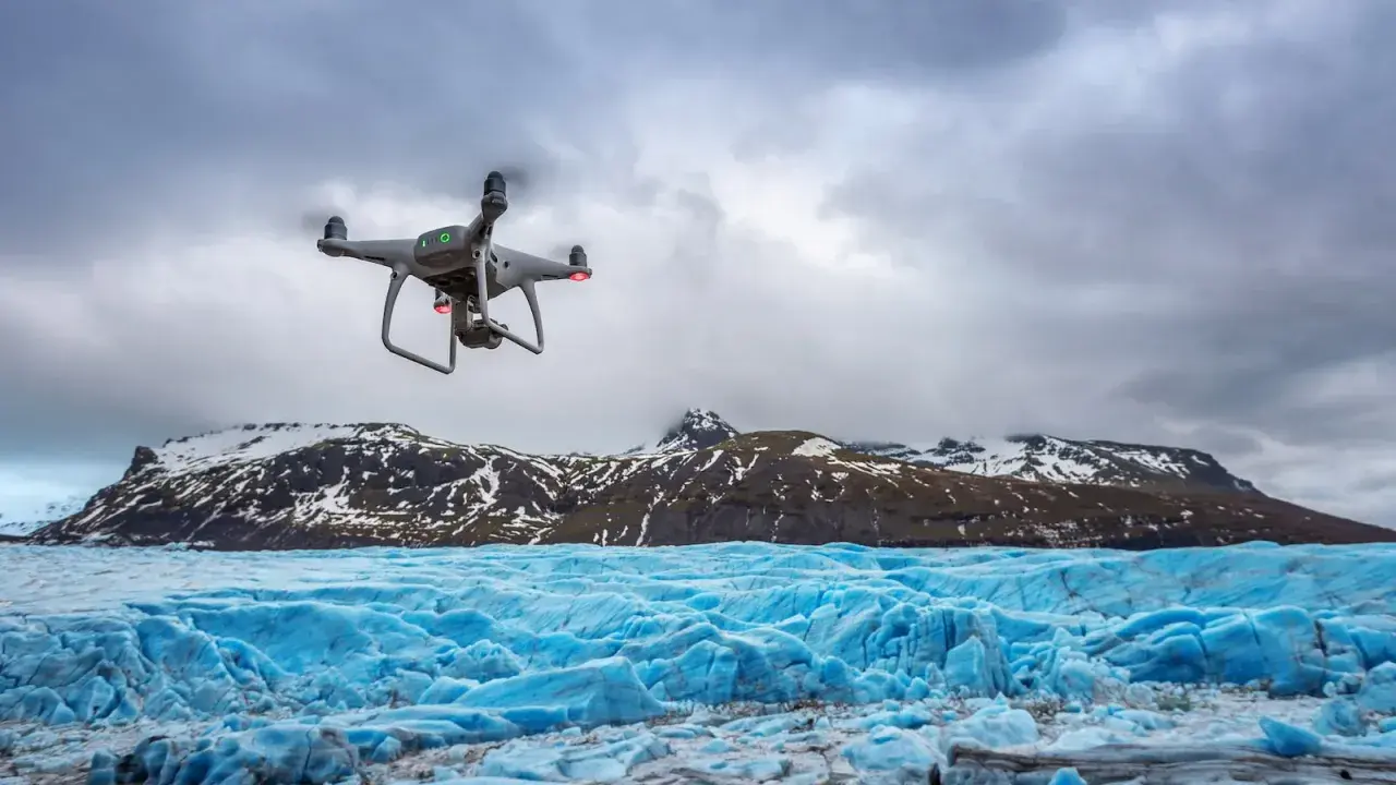 Dron lata nad lodowcem, tworząc niesamowite zdjęcia z drona. W tle góry pokryte śniegiem.