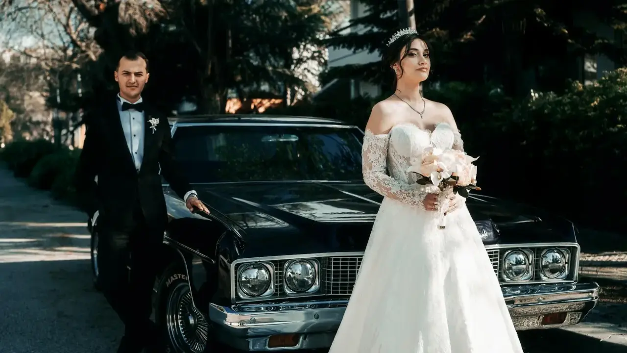 Para, w eleganckim czarnym garniturze, i panna młoda w sukni z koronki, z bukietem w dłoni, stoją obok zabytkowego samochodu. Nawet jeśli nie mam świadków na ślub, ten dzień jest nasz.