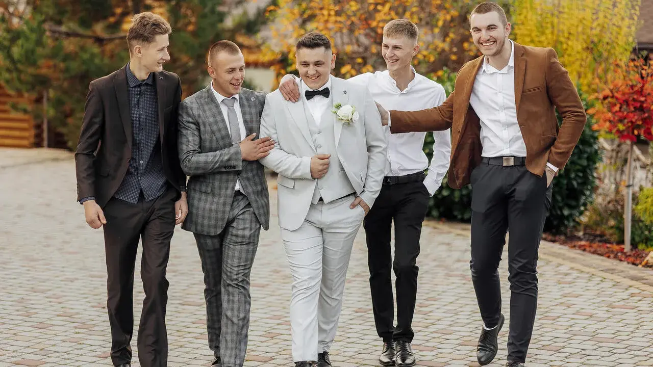Pięciu mężczyzn w eleganckich strojach, idealnych na wesele. Podpowiedź, jak ubrać się na wesele jako gość mężczyzna.