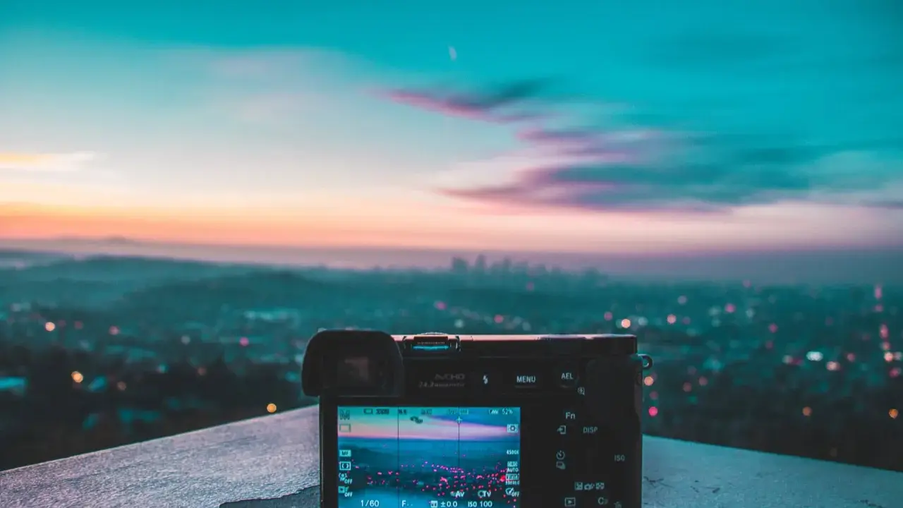 Aparat fotograficzny na tle miejskiego krajobrazu o zachodzie słońca. Różnorodne rodzaje światła tworzą magiczną atmosferę.