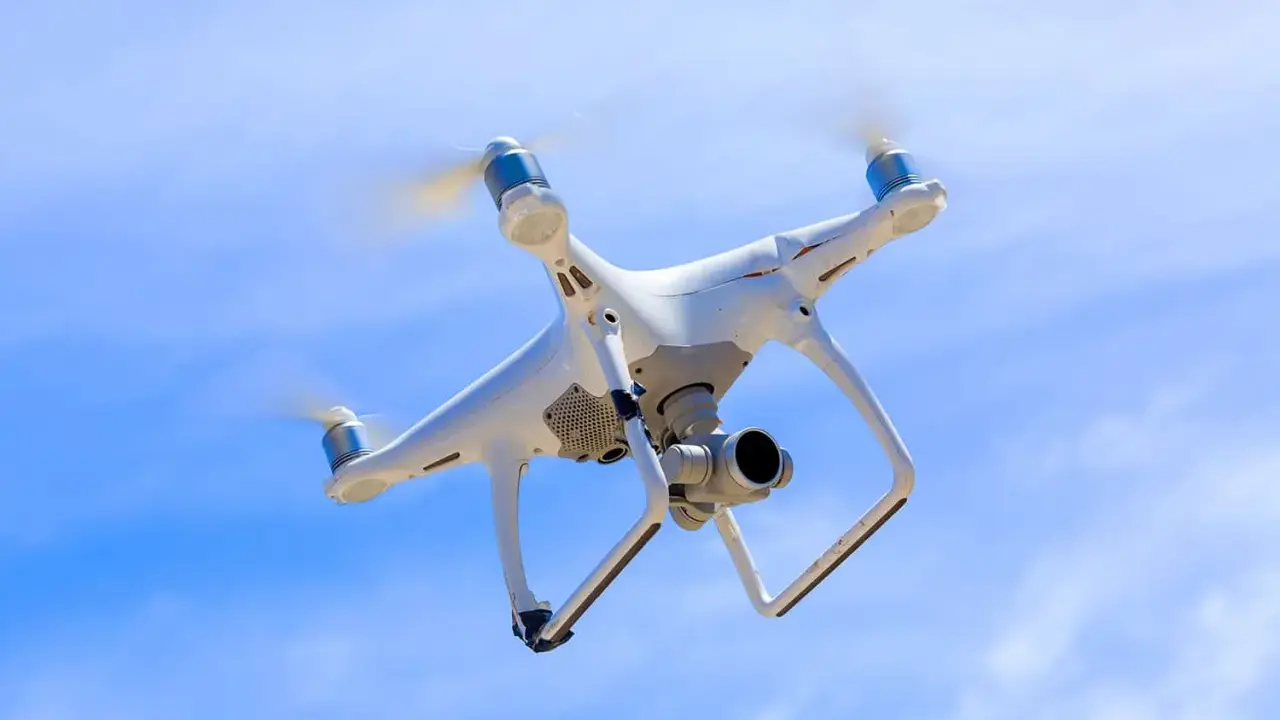 Biały dron z kamerą unosi się na tle błękitnego nieba.