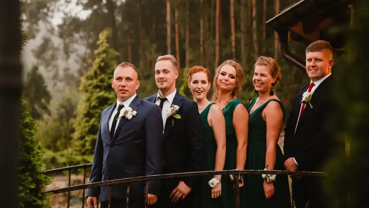 Pan młody i jego drużba, ubrani w garnitury, stoją obok druhen w zielonych sukniach. To idealna drużyna, która wie, co potrzebuje świadek do ślubu kościelnego.