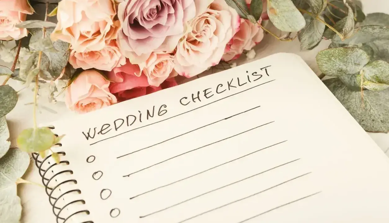 Bukiet róż i eukaliptusa obok notatnika z napisem "Wedding Checklist". Idealna inspiracja, co zabrać na wesele.