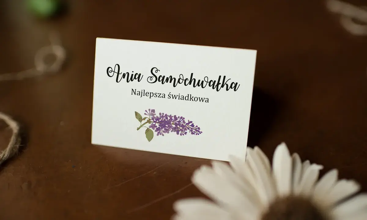 Winietka z napisem "Ania Samochwałka Najlepsza świadkowa" i gałązką bzu. Idealna inspiracja, jak wypisać winietki dla rodziców.
