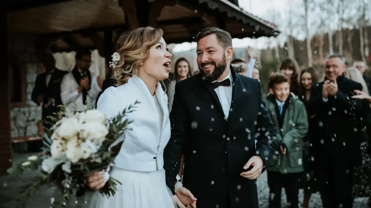 Szczęśliwa para młoda, trzymająca bukiet, wychodzi na zewnątrz podczas swojego ślubu w Adwencie. Sypią się na nich płatki.