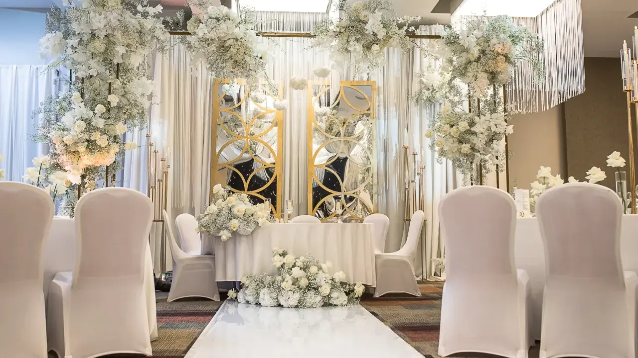 Eleganckie przyjęcie po ślubie cywilnym. Białe kwiaty, złote lustra i białe pokrowce na krzesłach tworzą romantyczną atmosferę.