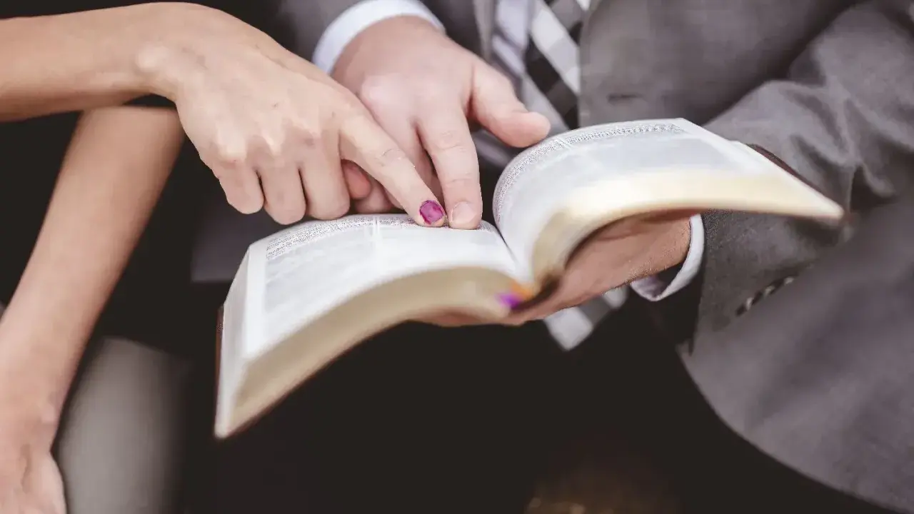 Dłonie pary wskazują na tekst w Biblii, przygotowując się do wspólnych czytań na ślubie.