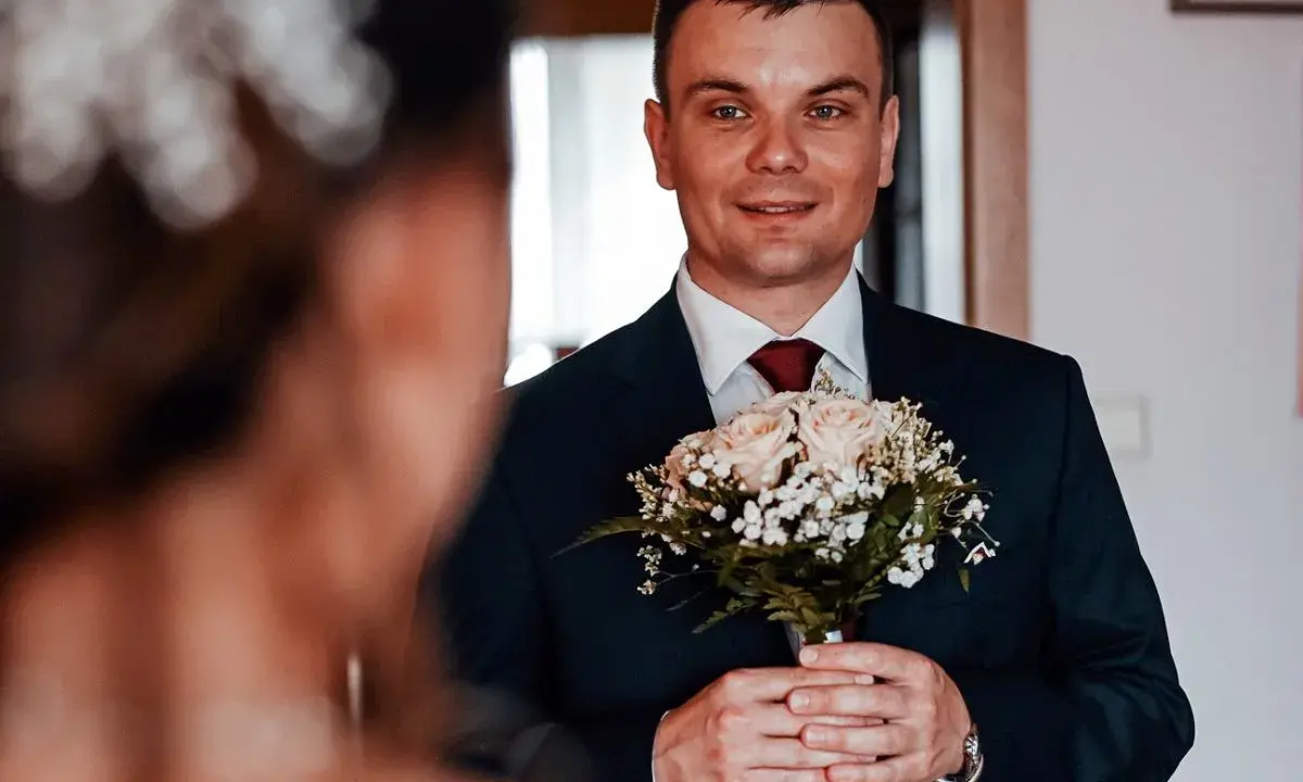 Młody mężczyzna w garniturze trzyma bukiet róż. Czy były ksiądz może wziąć ślub kościelny? To pytanie, które nurtuje wielu.