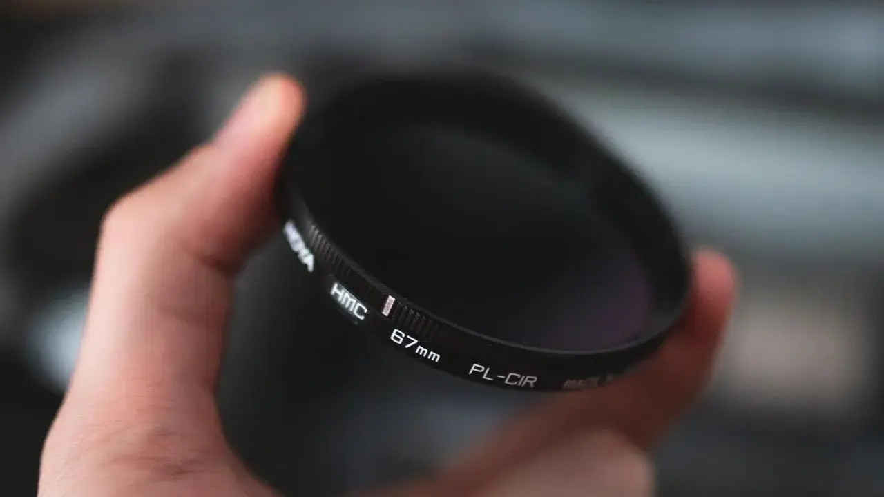 Dłoń trzyma okrągły filtr fotograficzny. To jeden z rodzajów filtrów fotograficznych, który pomaga uzyskać lepsze efekty.
