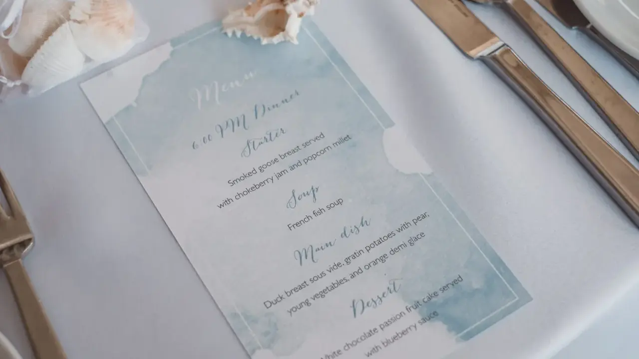 Menu weselne z akwarelowym motywem morskim, ozdobione muszlami.