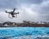 Dron lata nad lodowcem, tworząc niesamowite zdjęcia z drona. W tle góry pokryte śniegiem.