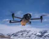 Mavic 4 Pro w locie, sterowany przez aplikację dji fly. W tle ośnieżone góry i błękitne niebo.