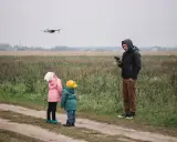 Ojciec steruje dronem, a dzieci z zaciekawieniem patrzą w niebo. Rodzinna przygoda z technologią w tle jesiennego krajobrazu.