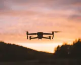 Dron w locie na tle zachodzącego słońca. Jego zasięg pozwala na uchwycenie pięknych krajobrazów.