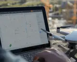 Planowanie zgłoszenie lotu dronem na mapie na laptopie. Obok leży dron.
