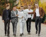 Pięciu mężczyzn w eleganckich strojach, idealnych na wesele. Podpowiedź, jak ubrać się na wesele jako gość mężczyzna.