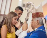Biskup udziela sakramentu bierzmowania młodej kobiecie. Czy do ślubu kościelnego potrzebne jest bierzmowanie? To pytanie nurtuje wiele par.