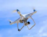 Biały dron z kamerą unosi się na tle błękitnego nieba.