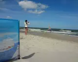 Dziewczyna robi fikołka na plaży, podczas gdy druga filmuje ją telefonem. Krzywy horyzont dodaje dynamiki scenie.