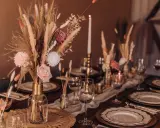 Stół weselny w stylu boho: bukiety z traw pampasowych, róże, świece i złote naczynia tworzą ciepłą atmosferę.