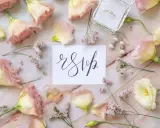 Delikatne kwiaty i biżuteria otaczają kartkę z napisem "rsvp".