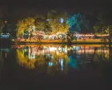 Nastrojowa fotografia nocna nad jeziorem, z oświetlonymi drzewami i budynkami, tworzącymi piękne odbicia w wodzie.