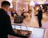 DJ przy konsoli na weselu. Młoda para tańczy na parkiecie. Zastanawiasz się, wesele ile za osobę?