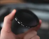 Dłoń trzyma okrągły filtr fotograficzny. To jeden z rodzajów filtrów fotograficznych, który pomaga uzyskać lepsze efekty.