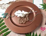 Winietki co to? Eleganckie winietki z imieniem "Monika Szpak" na liściu dębu, ozdobione sznurkiem i żołędziami, na brązowym talerzu.
