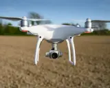 Biały dron DJI Phantom 4 Pro w locie nad polem.