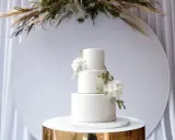 Elegancki, trójpoziomowy tort weselny w nowoczesnym stylu, ozdobiony białymi kwiatami i zielonymi liśćmi. Idealny na wyjątkowe okazje.