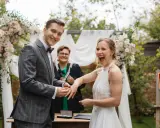 Szczęśliwa para podczas ceremonii ślubu cywilnego. Pan młody zakłada obrączkę pani młodej, która radośnie się śmieje.