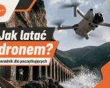 Poradnik "Jak latać dronem?" dla początkujących. Dron w locie nad malowniczym wybrzeżem z kamiennym akweduktem.