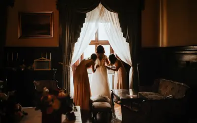 Panna młoda w sukni ślubnej, z pomocą druhen, przygotowuje się do ceremonii. To jej "coś pożyczonego na ślub".