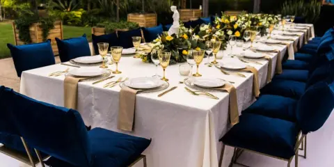 Elegancka sala bankietowa z białym obrusem, złotymi sztućcami i granatowymi krzesłami. To idealne miejsce na poprawiny, gdzie świętuje się dalszy ciąg wesela.