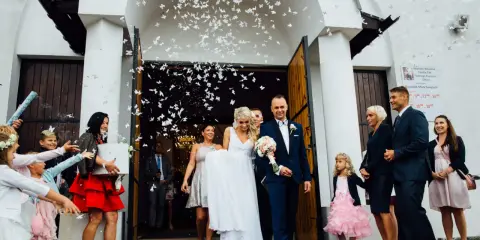 Para młoda wychodzi z kościoła, obsypana płatkami w kształcie motyli. To typowe polskie wesele, pełne radości i tradycji.