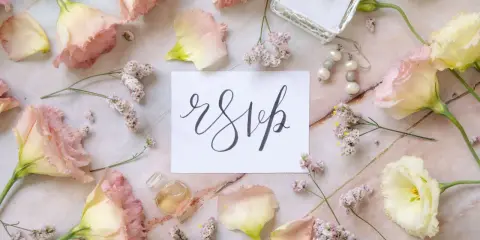 Delikatne kwiaty i biżuteria otaczają kartkę z napisem "rsvp".