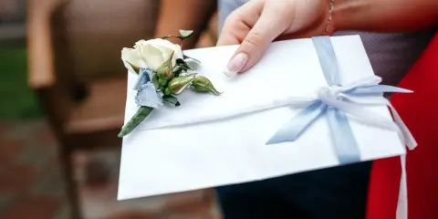 Biała koperta z błękitną wstążką i butonierką, symbolizująca pieniądze z wesela na konto.