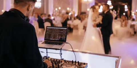 DJ przy konsoli na weselu. Młoda para tańczy na parkiecie. Zastanawiasz się, wesele ile za osobę?