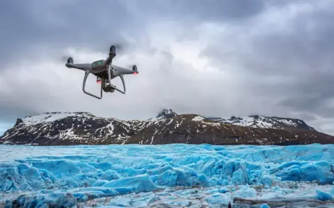 Dron lata nad lodowcem, tworząc niesamowite zdjęcia z drona. W tle góry pokryte śniegiem.