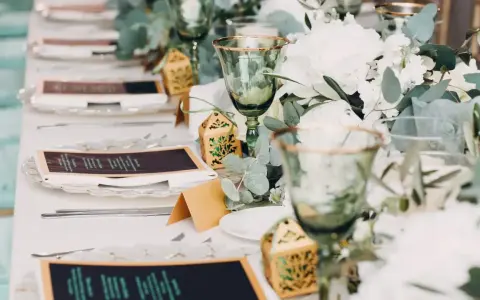 Eleganckie nakrycia stołu na wesele bez alkoholu: zielone kieliszki, menu, ozdobne pudełeczka i bukiety.