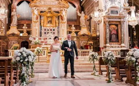 Para młoda idzie do ołtarza podczas ślubu w Rzymie. Wspaniała bazylika, ozdobiona kwiatami i organami, tworzy magiczną atmosferę.