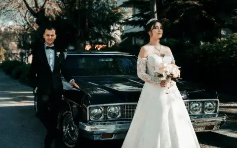 Para, w eleganckim czarnym garniturze, i panna młoda w sukni z koronki, z bukietem w dłoni, stoją obok zabytkowego samochodu. Nawet jeśli nie mam świadków na ślub, ten dzień jest nasz.