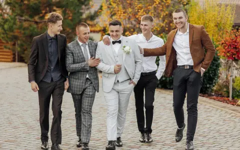 Pięciu mężczyzn w eleganckich strojach, idealnych na wesele. Podpowiedź, jak ubrać się na wesele jako gość mężczyzna.