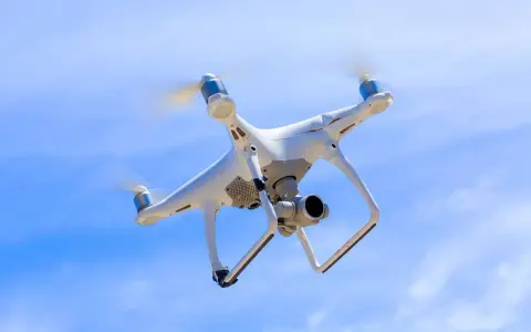 Biały dron z kamerą unosi się na tle błękitnego nieba.