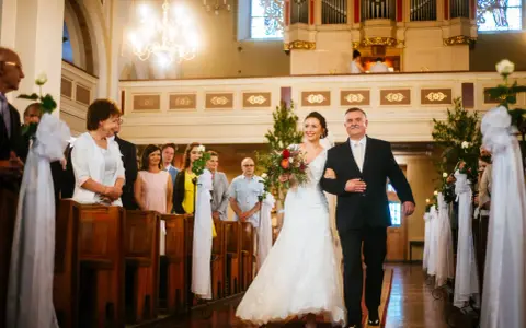 Panna młoda z bukietem idzie do ołtarza z ojcem. Cichy ślub kościelny bez mszy, w kościele pełnym gości.