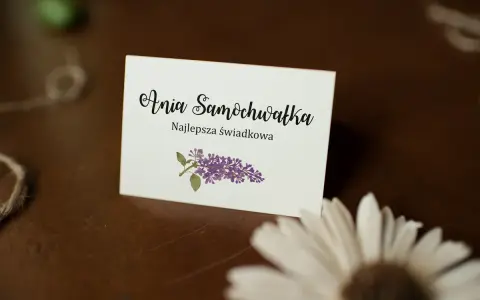 Winietka z napisem "Ania Samochwałka Najlepsza świadkowa" i gałązką bzu. Idealna inspiracja, jak wypisać winietki dla rodziców.