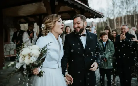 Szczęśliwa para młoda, trzymająca bukiet, wychodzi na zewnątrz podczas swojego ślubu w Adwencie. Sypią się na nich płatki.
