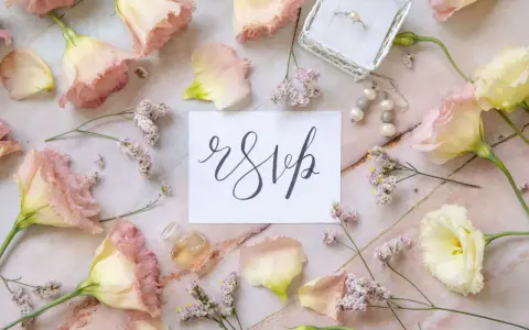 Delikatne kwiaty i biżuteria otaczają kartkę z napisem "rsvp".