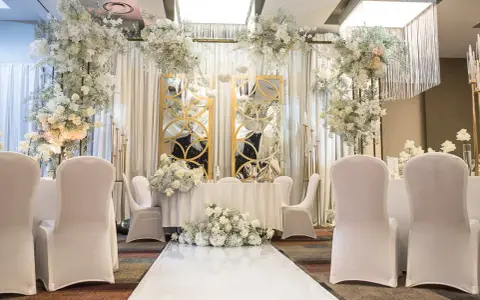 Eleganckie przyjęcie po ślubie cywilnym. Białe kwiaty, złote lustra i białe pokrowce na krzesłach tworzą romantyczną atmosferę.